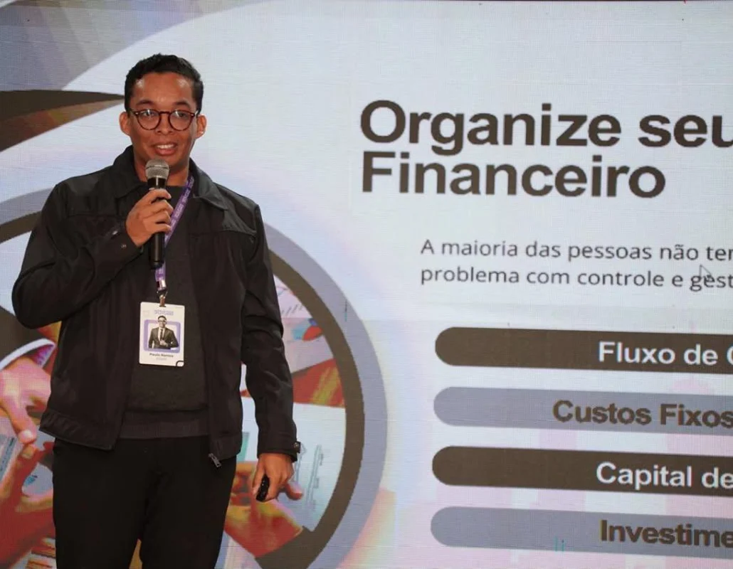 Paulo Ramos ao microfone durante palestra, diante de um slide sobre organização financeira.