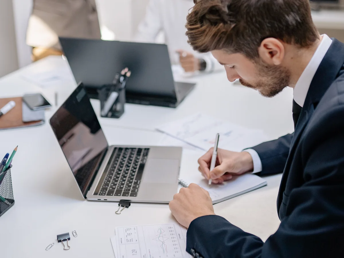 Equipe reunida em uma mesa, analisando relatórios impressos e telas de notebook.